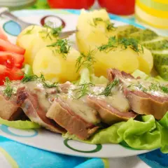 Jak przygotować ozorki: plastry ozorków w sosie, ziemniaki, pomidory i ogórki na talerzu.