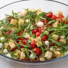 Pyszna sałatka z grzankami i parmezanem, pełna pomidorków koktajlowych, mozzarelli i rukoli.