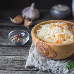 Kapusta kiszona w drewnianej misce, obok przyprawy i czosnek. Jak odróżnić objawy zepsutej kapusty kiszonej od prawidłowej fermentacji.