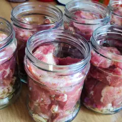 Słoiki z surowym mięsem, przygotowane do pasteryzacji gulaszu. Mięso jest pokrojone w kostkę i doprawione.