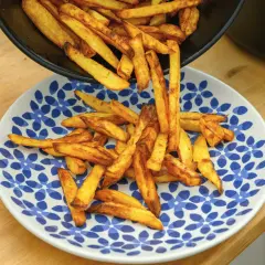 Złociste frytki, od cienkich shoestring po grubsze steak fries, wysypują się z patelni na talerz.