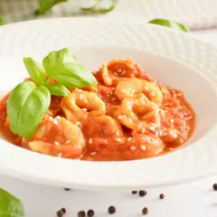 Pyszne tortellini w sosie pomidorowym, posypane sezamem i udekorowane listkami bazylii.