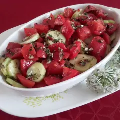 Sałatka z pomidorów i ogórków, doprawiona zbyt wcześnie, zaczyna puszczać sok. Obok ozdobne kwiaty czosnku.