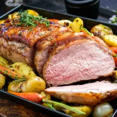 Soczysta polędwiczka wieprzowa pieczona w piekarniku z ziemniakami i marchewką, udekorowana ziołami.