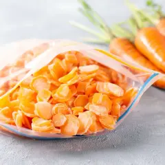 Mrożona, pokrojona marchewka w woreczku, obok świeżych korzeni. Warto mrozić tartą marchewkę na zapas do surówek, by mieć ją zawsze pod ręką.