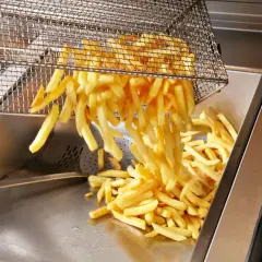 Frytki wysypywane z kosza do frytownicy. Nadmiar cukru w ziemniaku może powodować ciemnienie frytek podczas smażenia.