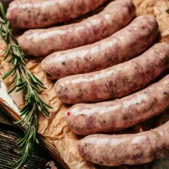 Surowa biała kiełbasa na desce, obok gałązki rozmarynu i papryczki chili. Czy można mrozić białą kiełbasę? Tak, można ją mrozić.