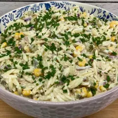 Pyszna sałatka z tuńczykiem i makaronem orzo, z kukurydzą i szczypiorkiem, w ozdobnej misce.