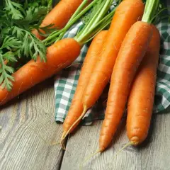 Świeże marchewki na drewnianym stole. Dowiedz się, jakie są przyczyny mięknięcia marchewki w surówce i jak zachować jej jędrność.
