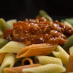 Kolorowy makaron penne z sosem bolońskim. Dowiedz się, jak dobrać sos do makaronu spaghetti a penne, zasady przywierania.