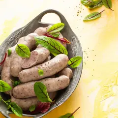 Domowa biała kiełbasa bez maszynki, podana w metalowej misie z liśćmi szczawiu.