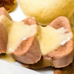 Pokrojone w plastry ozory wieprzowe w sosie, obok bułeczek. Jak wyciąć ślinianki w ozorach wieprzowych?