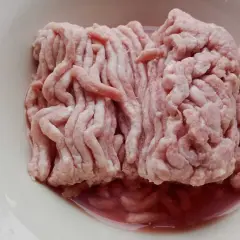 Mięso mielone w misce. Zwróć uwagę na podejrzany kolor i płyn, by rozpoznać objawy zepsutego mięsa mielonego.