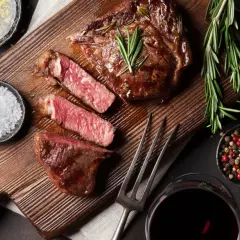 Soczysty rump steak, idealnie wysmażony, z gałązkami rozmarynu, solą i pieprzem. Obok kieliszek czerwonego wina.