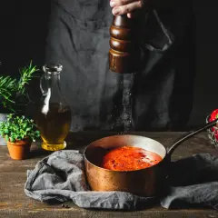 Gotujesz sos pomidorowy i zastanawiasz się, jak zneutralizować smak, gdy jest za słony? Na stole zioła, oliwa i papryczki.