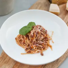 Porcja spaghetti z sosem bolognese, posypana parmezanem i udekorowana bazylią. Idealne danie, gdy chcesz wiedzieć, jak zawekować sos bolognese na później.