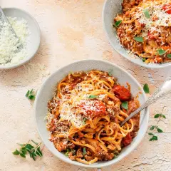 Dwa talerze spaghetti bolognese, posypane parmezanem. Obok miseczka z tartym serem i tarka. Długie gotowanie sosu to klucz do głębi smaku.
