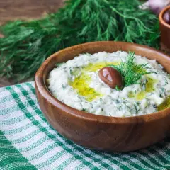 Oryginalny przepis na sos tzatziki: kremowy jogurt, świeży ogórek, czosnek, koperek i oliwa, ozdobiony oliwką.