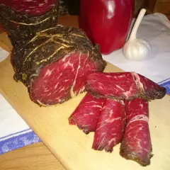Pokrojona wołowina w paski na desce, obok papryka i czosnek. Idealna do dalszej obróbki, jak kroić wołowinę w paski.