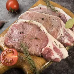 Surowe kotlety schabowe z przyprawami, gałązkami rozmarynu, czosnkiem i pomidorem. Zastanawiasz się, jak długo wędzić schab bez parzenia?