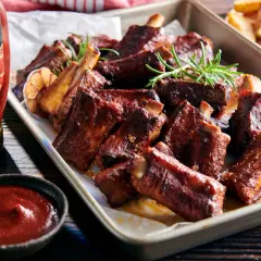 Soczyste żeberka BBQ z czosnkiem i rozmarynem, idealnie pasują do żeberek, a obok sos i frytki.