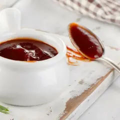 Pyszny, gęsty sos barbecue w białej sosjerce i na łyżce. Idealny przykład, jak zrobić sosy, które wzbogacą każde danie.