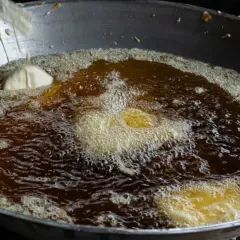 Jak sprawdzić temperaturę oleju bez termometru metodą z drewnianą łyżką? Widać bulgoczący olej i kawałek ciasta w głębokim tłuszczu.