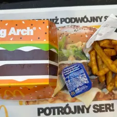 Duże frytki McDonald's w papierowym opakowaniu obok pudełka Big Arch i sosu.