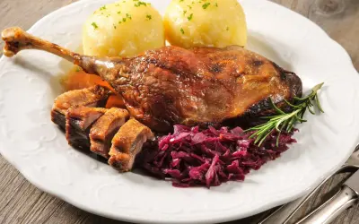 Pieczona kaczka z kluskami, czerwoną kapustą i rozmarynem na białym talerzu.