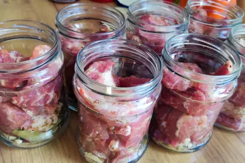 Słoiki z surowym mięsem, przygotowane do pasteryzacji gulaszu. Mięso jest pokrojone w kostkę i doprawione.