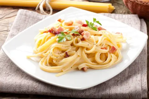 Pyszne spaghetti carbonara, przygotowane według oryginalnego przepisu, z chrupiącym boczkiem i świeżą natką pietruszki.