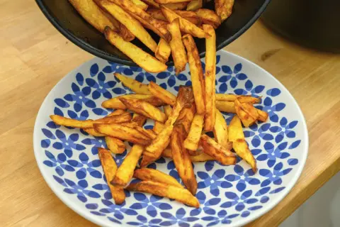 Złociste frytki, od cienkich shoestring po grubsze steak fries, wysypują się z patelni na talerz.
