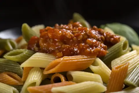 Kolorowy makaron penne z sosem bolońskim. Dowiedz się, jak dobrać sos do makaronu spaghetti a penne, zasady przywierania.
