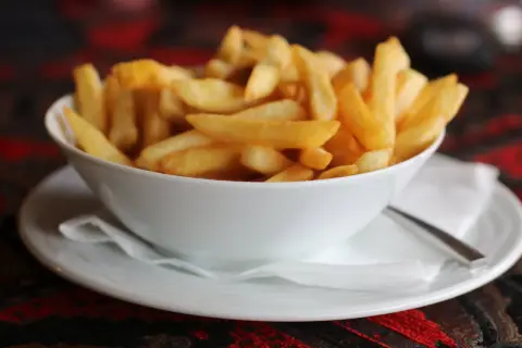 Chrupiące frytki domowe jak z restauracji krok po kroku. Złociste, idealne ziemniaczki w białej miseczce.