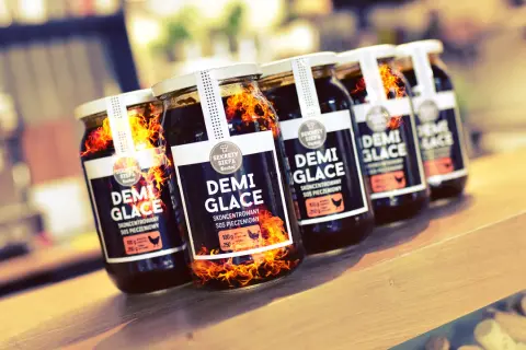 Słoiki z sosem demi-glace, jak zrobić idealny sos demi-glace bez 48 godzin gotowania. Płomienie sugerują intensywny smak.