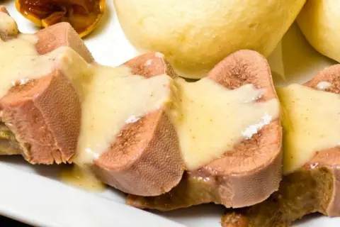 Pokrojone w plastry ozory wieprzowe w sosie, obok bułeczek. Jak wyciąć ślinianki w ozorach wieprzowych?