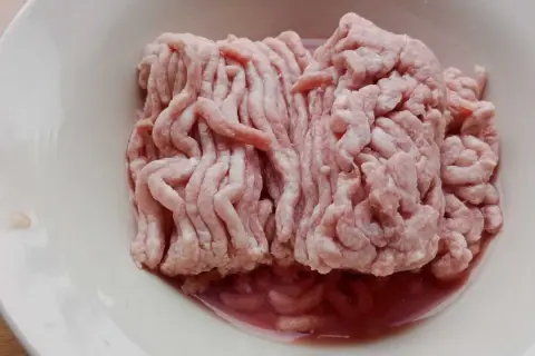 Mięso mielone w misce. Zwróć uwagę na podejrzany kolor i płyn, by rozpoznać objawy zepsutego mięsa mielonego.