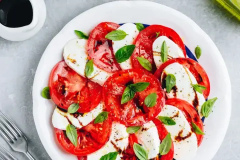 Sałatka caprese z pomidorami i mozzarellą. Woda w sałatce może pojawić się z powodu dojrzałości pomidorów lub nadmiaru sosu.
