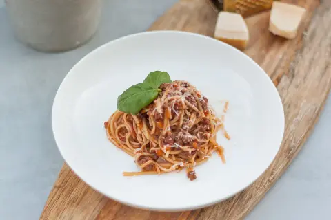 Porcja spaghetti z sosem bolognese, posypana parmezanem i udekorowana bazylią. Idealne danie, gdy chcesz wiedzieć, jak zawekować sos bolognese na później.