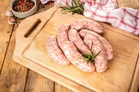 Surowa biała kiełbasa na desce, gotowa do przyrządzenia. Dowiedz się, jak długo gotować białą kiełbasę, by była idealna.