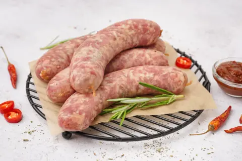 Surowa biała kiełbasa na ruszcie, gotowa do przygotowania. Obok papryczki chili i sos. Idealna do gotowania.