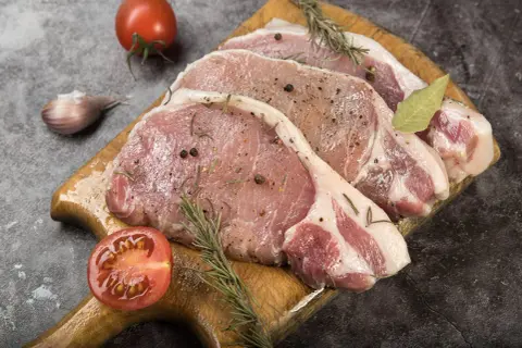 Surowe kotlety schabowe z przyprawami, gałązkami rozmarynu, czosnkiem i pomidorem. Zastanawiasz się, jak długo wędzić schab bez parzenia?