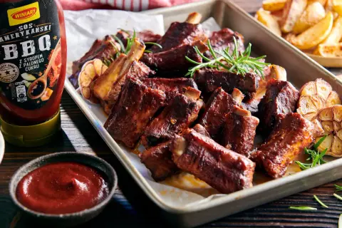 Soczyste żeberka BBQ z czosnkiem i rozmarynem, idealnie pasują do żeberek, a obok sos i frytki.