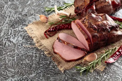 Wędzony schab, pokrojony w plastry, z czosnkiem, rozmarynem i papryczkami chili. Idealny przykład, jak zamarynować schab do wędzenia.