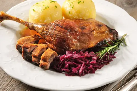 Pieczona kaczka z kluskami, czerwoną kapustą i rozmarynem na białym talerzu.