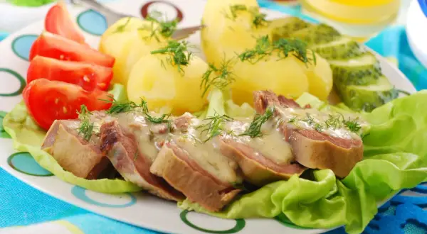 Jak przygotować ozorki: plastry ozorków w sosie, ziemniaki, pomidory i ogórki na talerzu.
