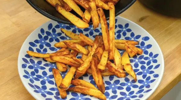 Złociste frytki, od cienkich shoestring po grubsze steak fries, wysypują się z patelni na talerz.