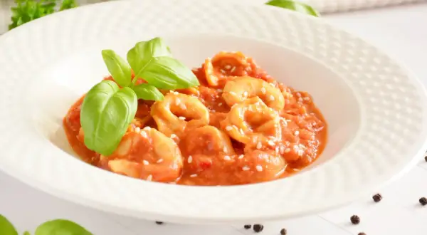 Pyszne tortellini w sosie pomidorowym, posypane sezamem i udekorowane listkami bazylii.