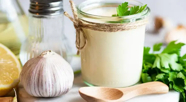 Sos aioli w słoiku, czosnek, cytryna i zioła. Różnica między sosem aioli a klasycznym majonezem czosnkowym jest subtelna, ale wyczuwalna.