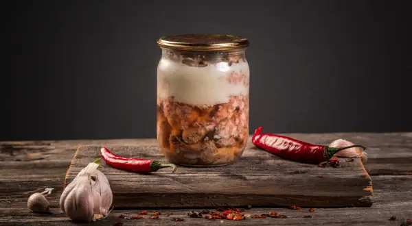 Słoik z mięsnym sosem do spaghetti, obok papryczki chili i czosnku. Czy można zawekować sos do spaghetti z mięsem? Tak, to świetny sposób na jego przechowywanie.
